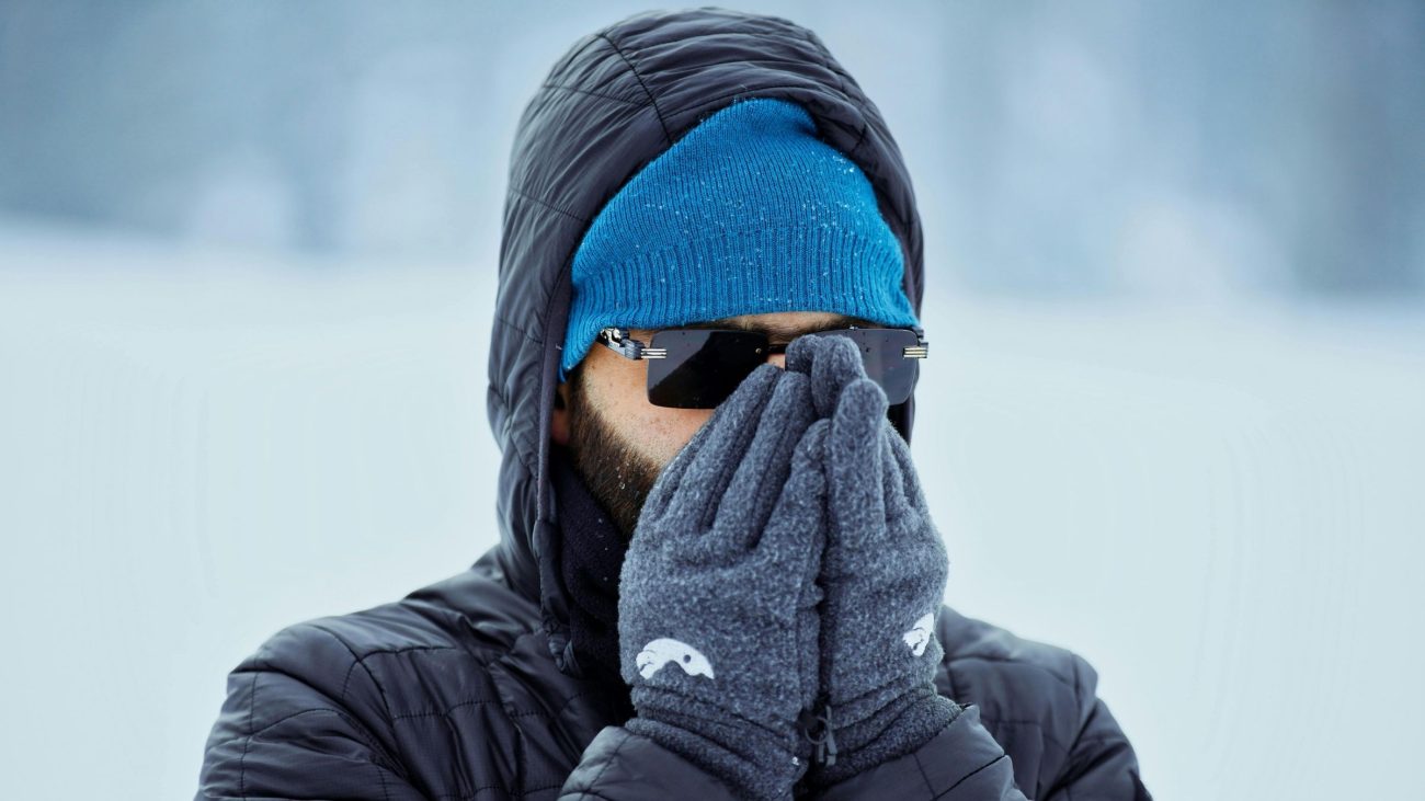 Pessoa agasalhada com gorro, luvas e óculos protege o rosto do frio intenso em ambiente de inverno